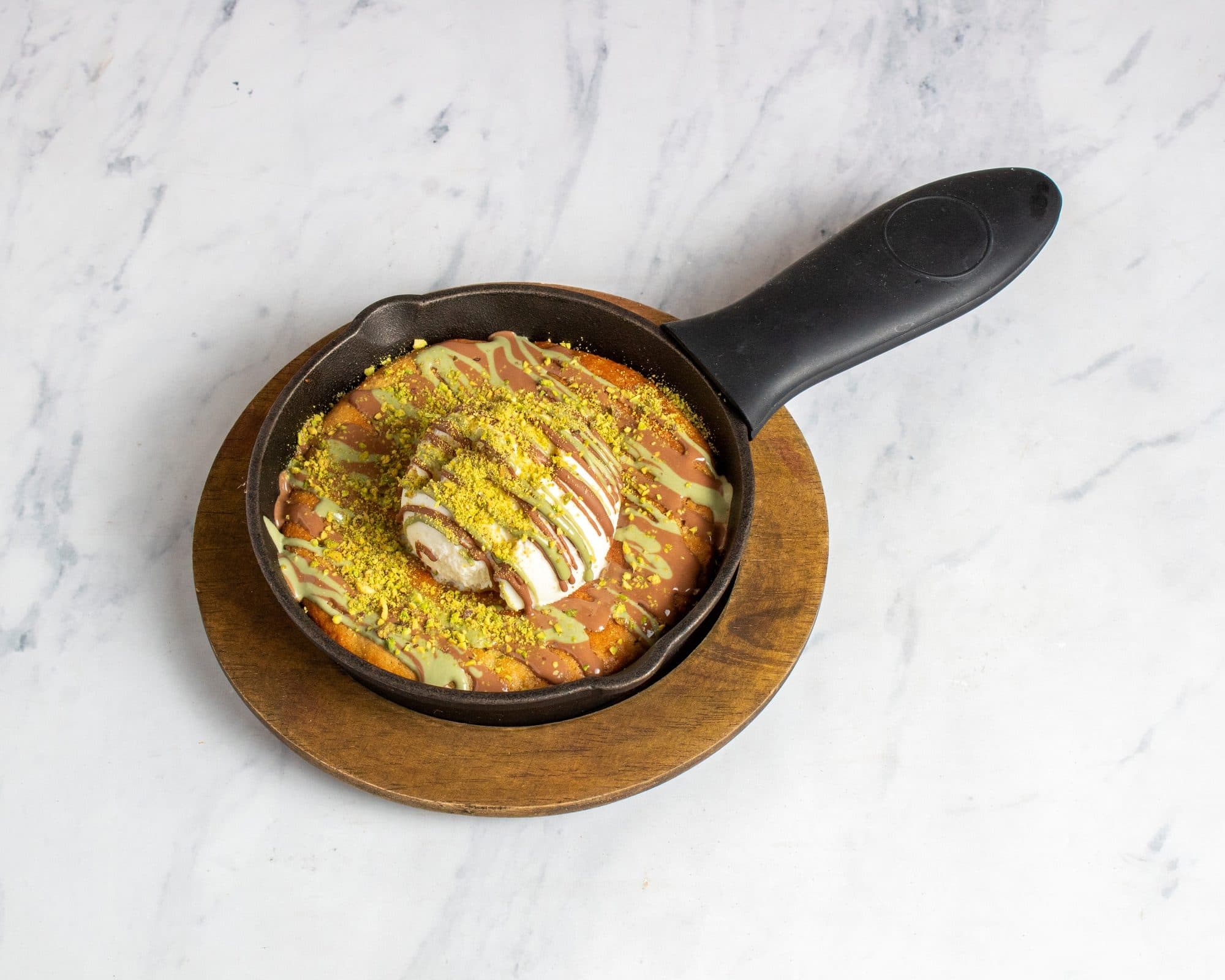 A skillet cookie with pistachio drizzle under a scoop of vanilla ice cream