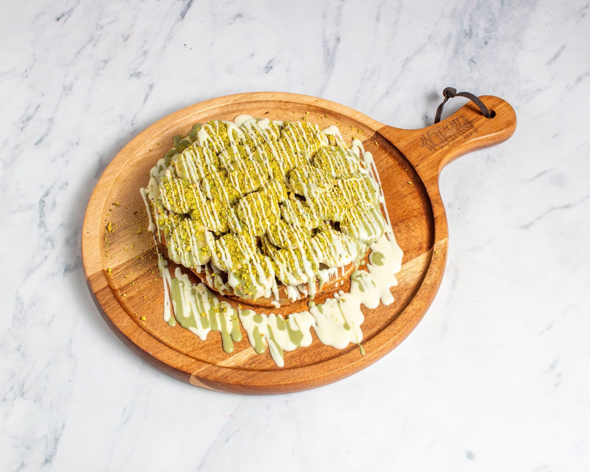 A waffle topped with banana, pistachio crumble, and white chocolate