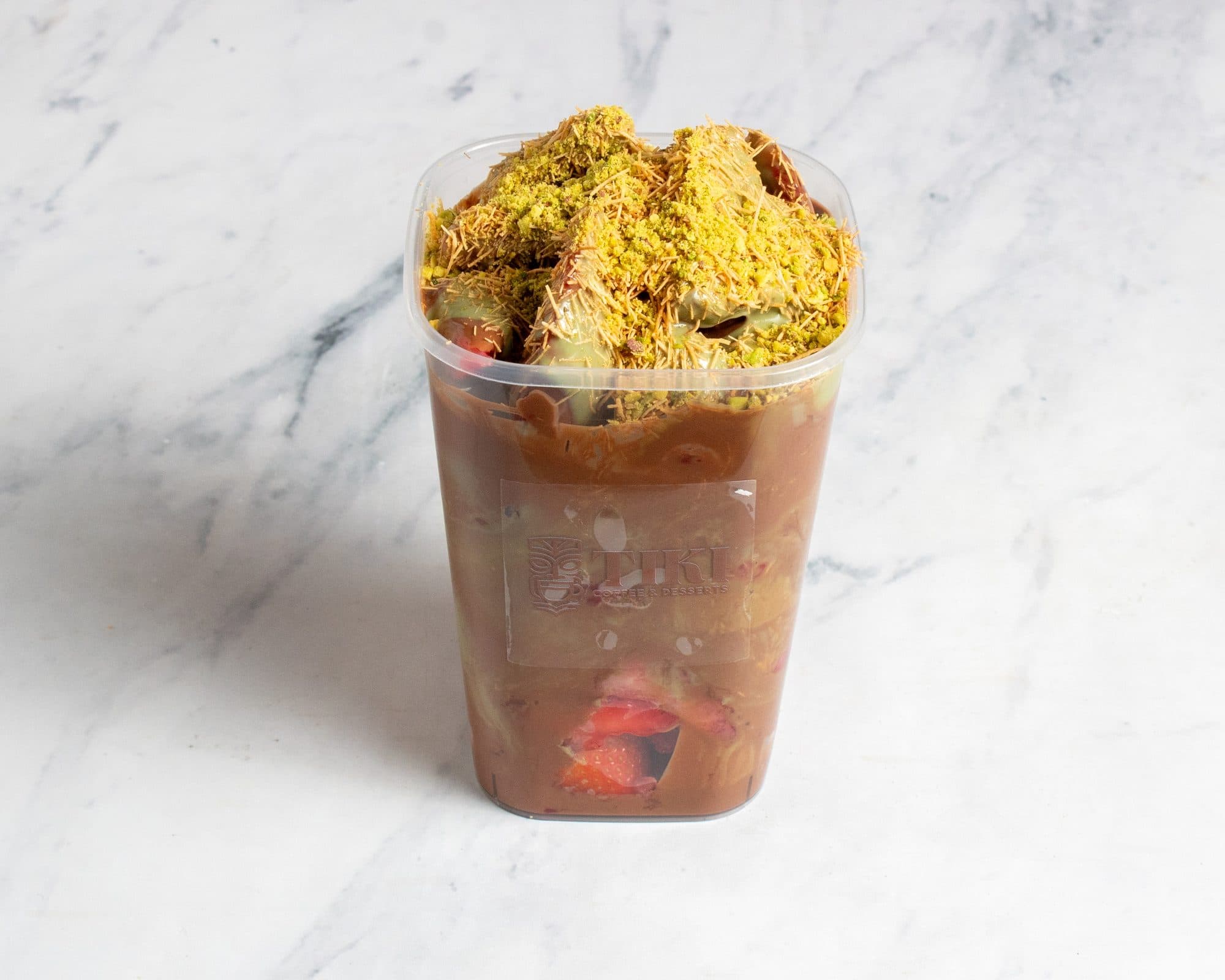 A layered dessert cup of chocolate, strawberries, knafa, and pistachio