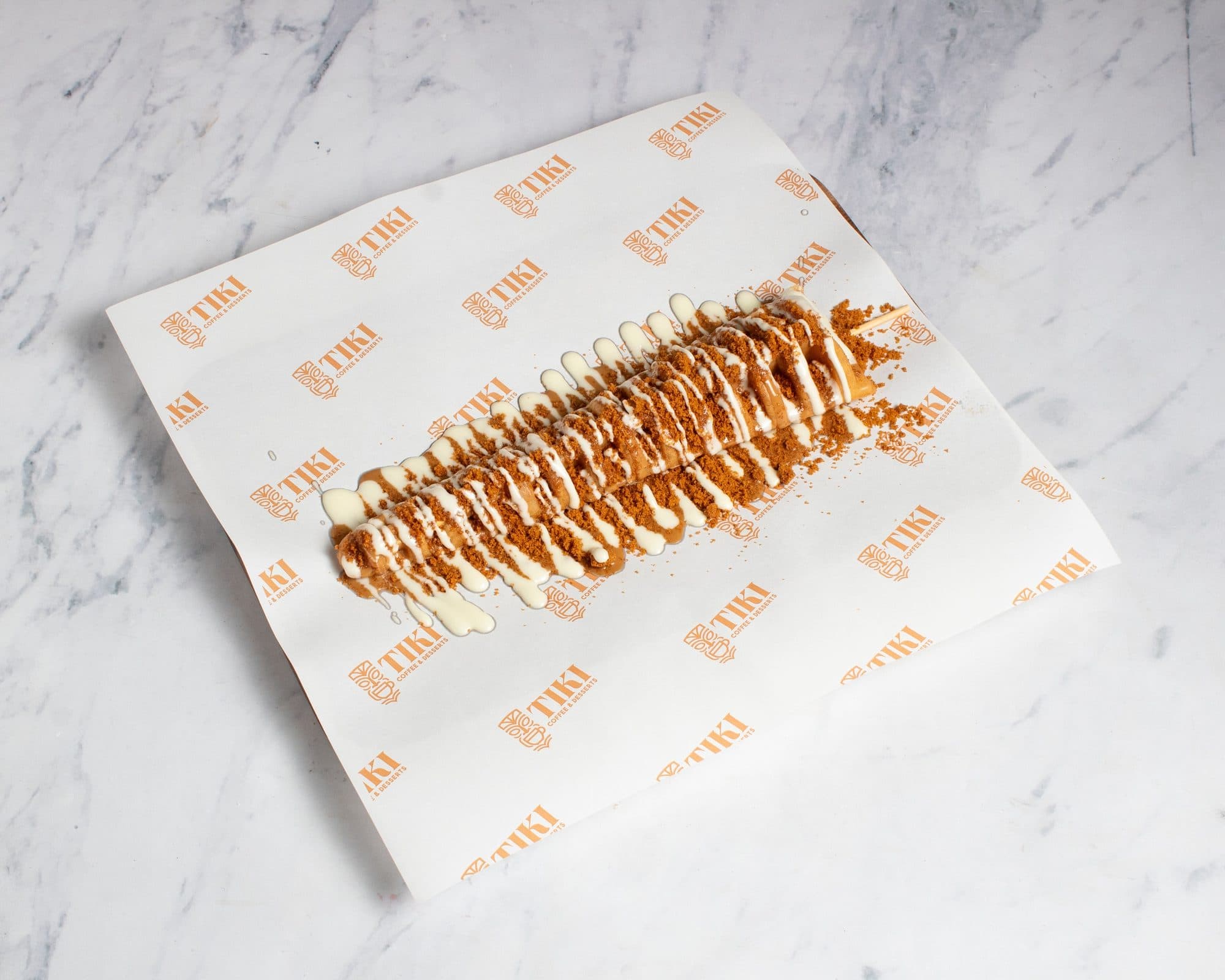A waffle on a stick under white chocolate drizzle and Lotus crumble
